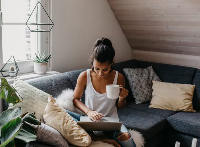 Frau mit Teetasse und Notebook auf Sofa